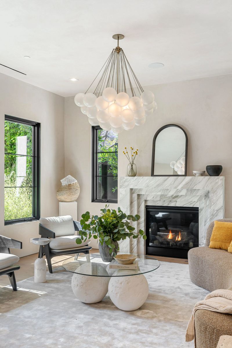 Modern living room with elegant chandelier, marble fireplace, and stylish decor, featuring a glass table and cozy seating.