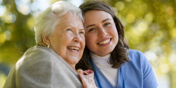 Smiling elderly woman with a young nurse outside.