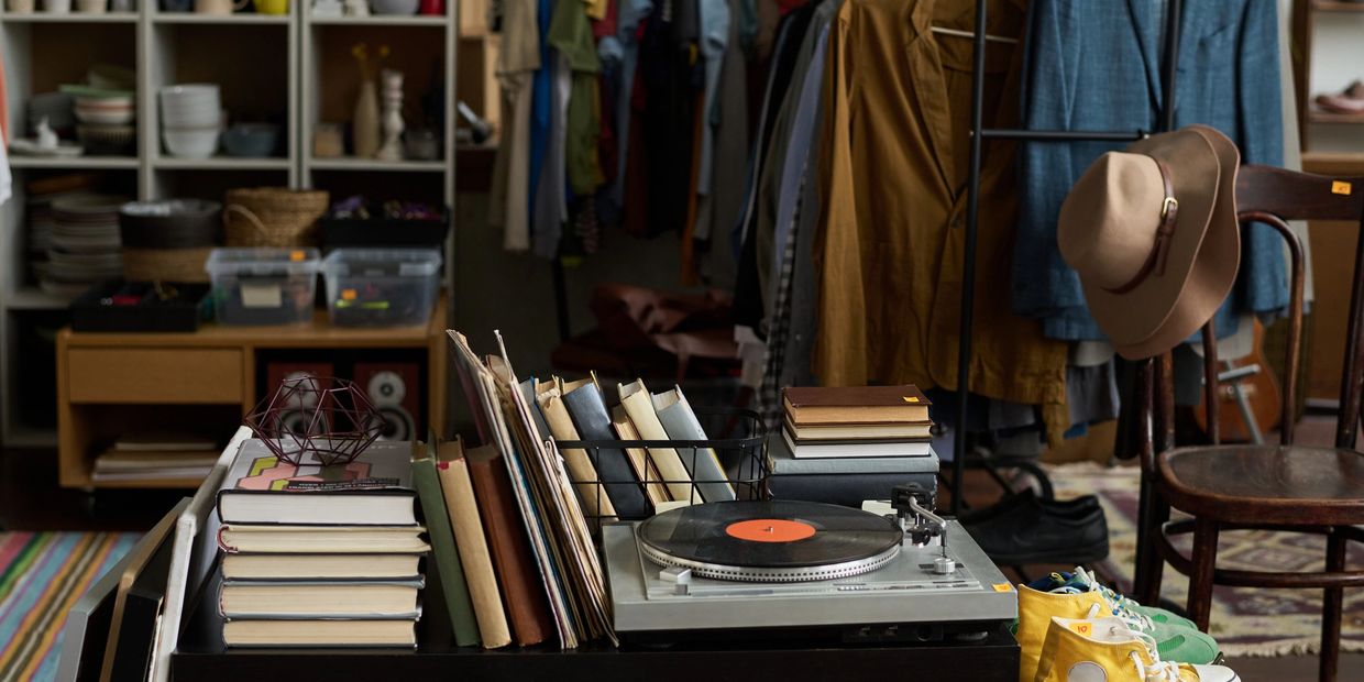Vintage record player with books, clothing, and shoes in a cozy thrift store.