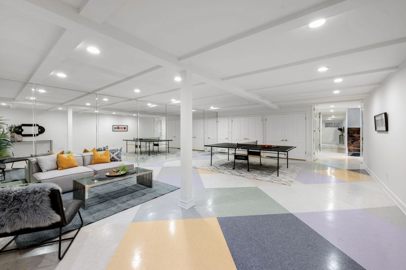 A modern basement interior featuring a ping pong table and cozy seating area with colorful flooring