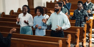 Hands clasped in prayer on a Bible during a group gathering.