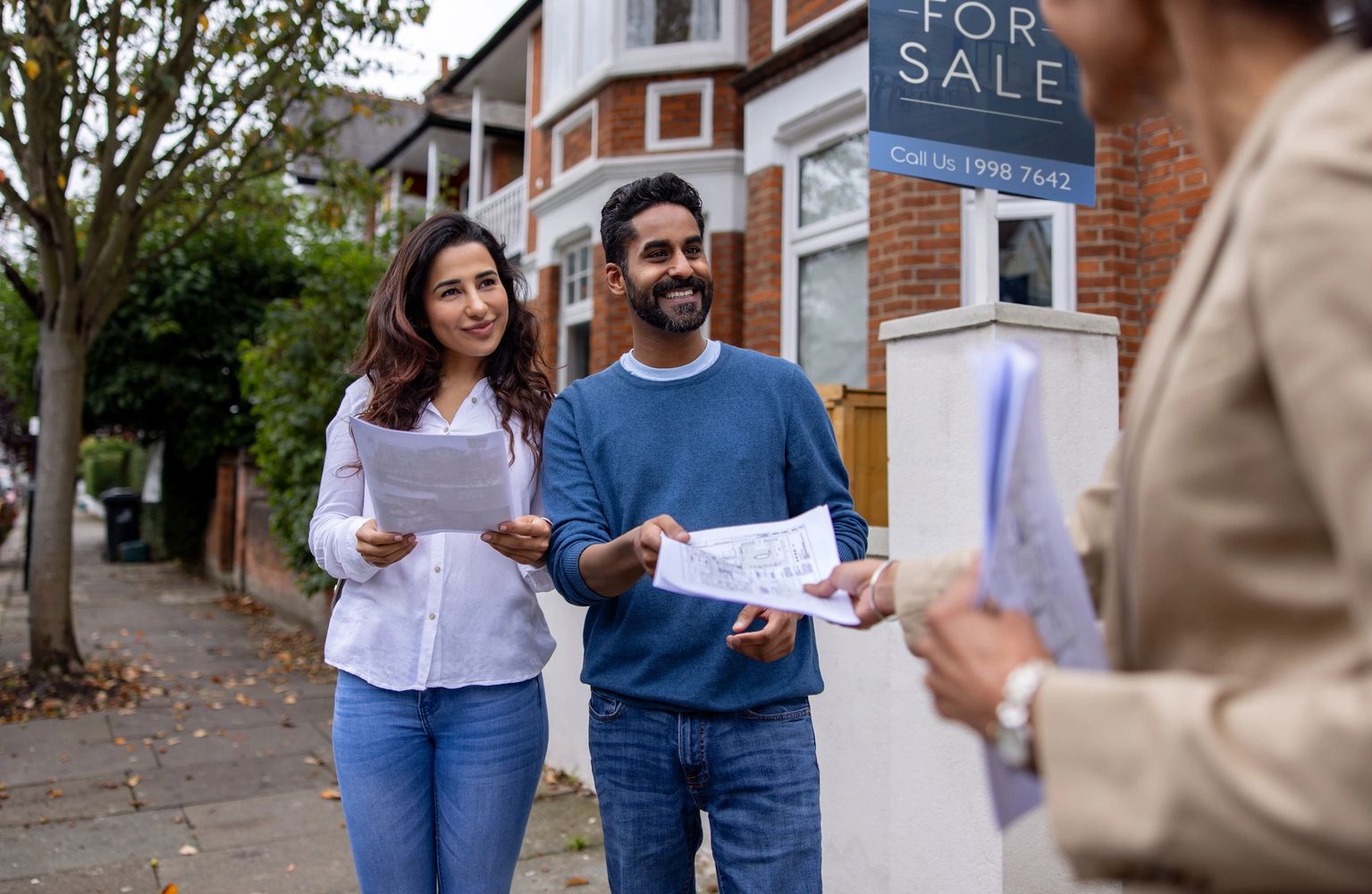 Happy couple reviewing property documents outside a house for sale.