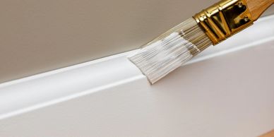 A paintbrush applying white paint on molding.