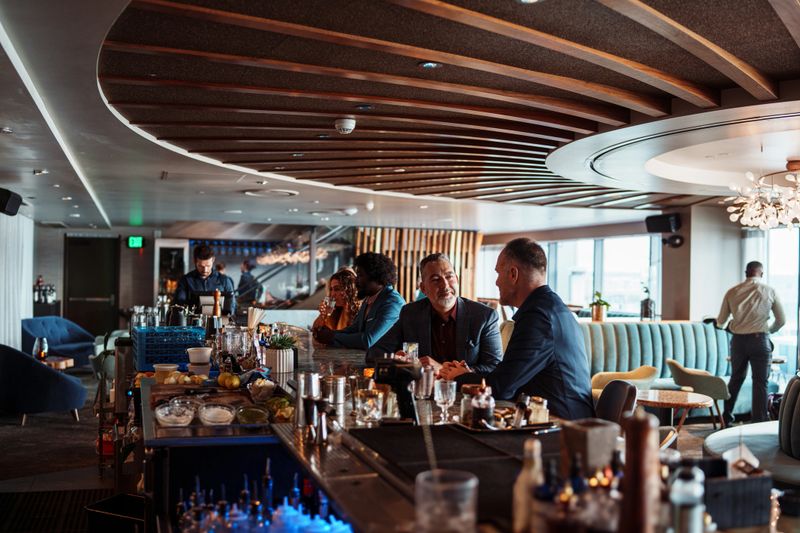 A handsome man sits at the bar of an upscale restaurant and chats with his husband.