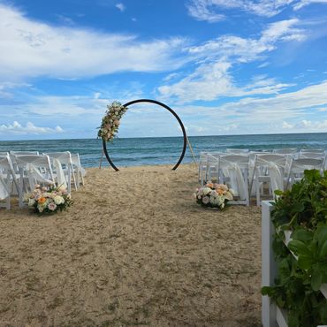 Beach wedding setup with floral decorations and a circular arch.