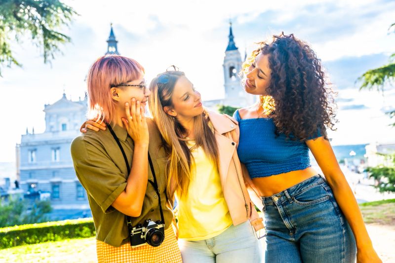 Portrait of three cute female caucasian and hispanic travelers enjoying sunset on city viewpoint in Madrid