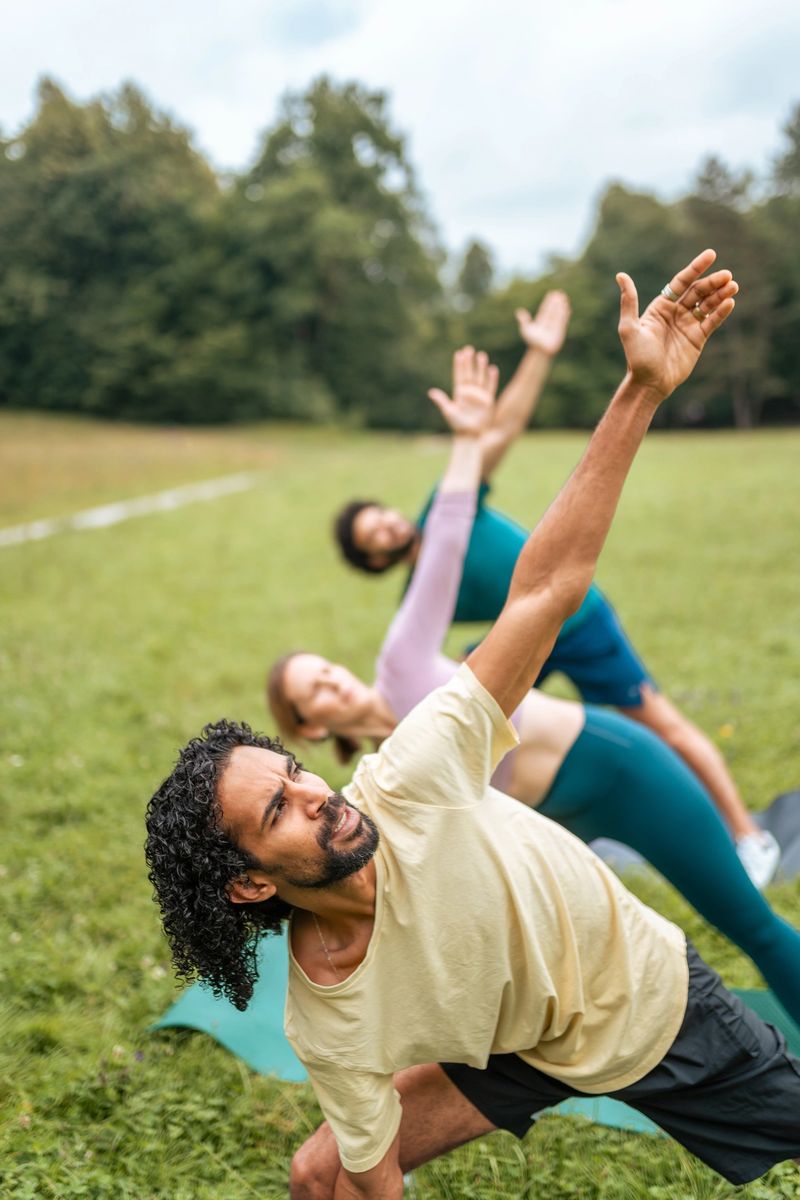 Men and women of varying ethnicities perform yoga outdoors, clad in comfortable athletic wear, surrounded by greenery, enhancing their wellness with every pose.