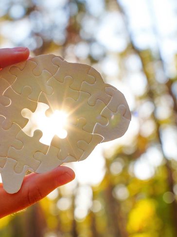 Hand holding brain-shaped puzzle with a missing piece and sunlight shining through.