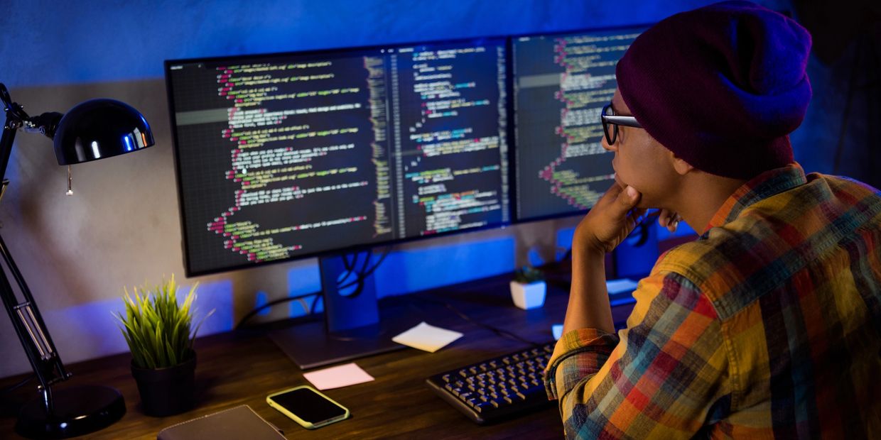 Person coding on dual monitors in a dimly lit room.