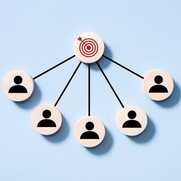 Wooden tokens showing teamwork towards a central target on a blue background.