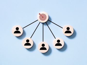 Wooden tokens showing teamwork towards a central target on a blue background.