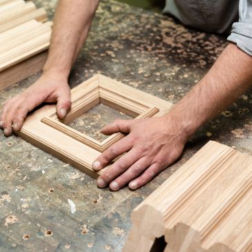 Hands working on wooden frames on a workbench.