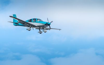 Single-engine propeller aircraft flying through a partly cloudy sky with blue and white gradient.