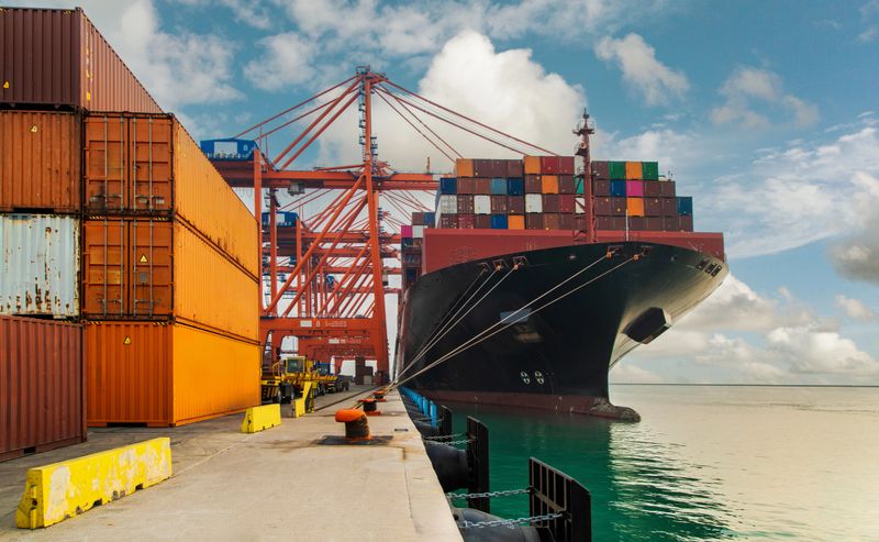 Cargo container ship moored at harbor. Loading or unloading containers with cranes.