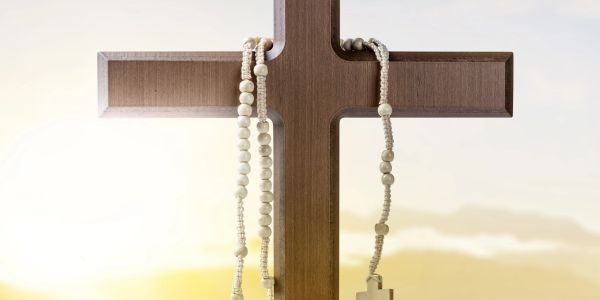 Wooden cross with rosary beads at sunrise.