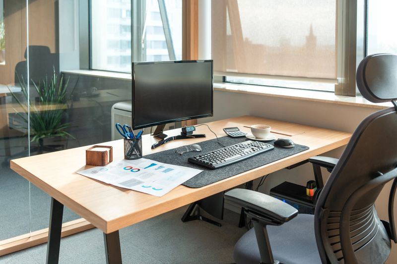A neatly organized office workspace featuring a desktop computer, ergonomic chair, and assorted office supplies, with natural light streaming through the window.