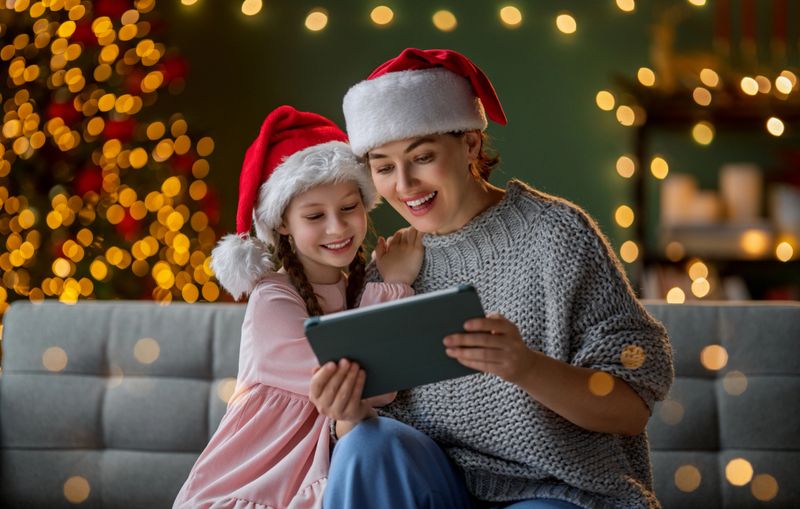 Merry Christmas and Happy Holidays. Mother and child using tablet pc. Parents and daughters having fun near tree indoors. Loving family in the room.