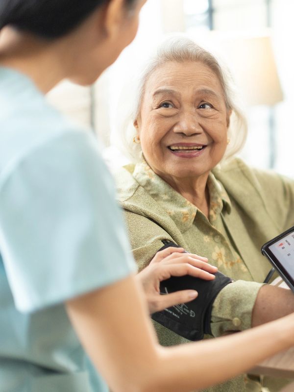Nurse checking elderly woman's blood pressure with a digital monitor.