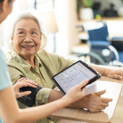 Elderly woman smiling while a healthcare worker checks her blood pressure with a digital device.