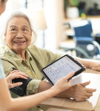 Elderly woman smiling while having her blood pressure checked with a digital monitor.