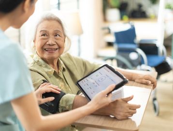 Elderly woman smiling while a caregiver shows her a tablet.