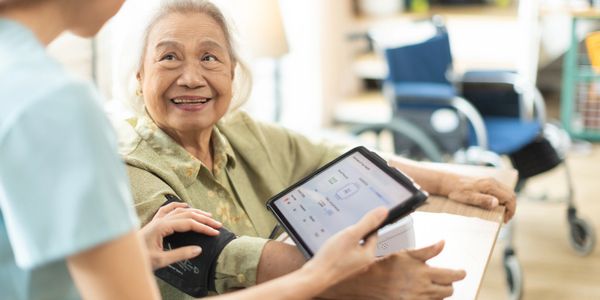 Nurse checking elderly woman's blood pressure with a digital monitor.
