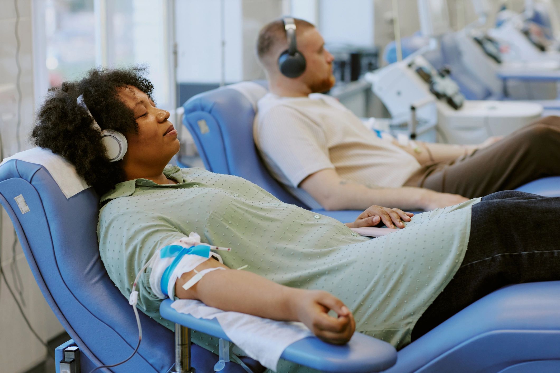 Two people donating blood while wearing headphones.