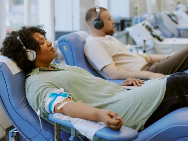 Two people donating blood while relaxing with headphones.