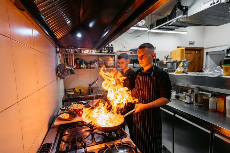 Young male chef and sous-chef cooking with fire in a commercial kitchen.
