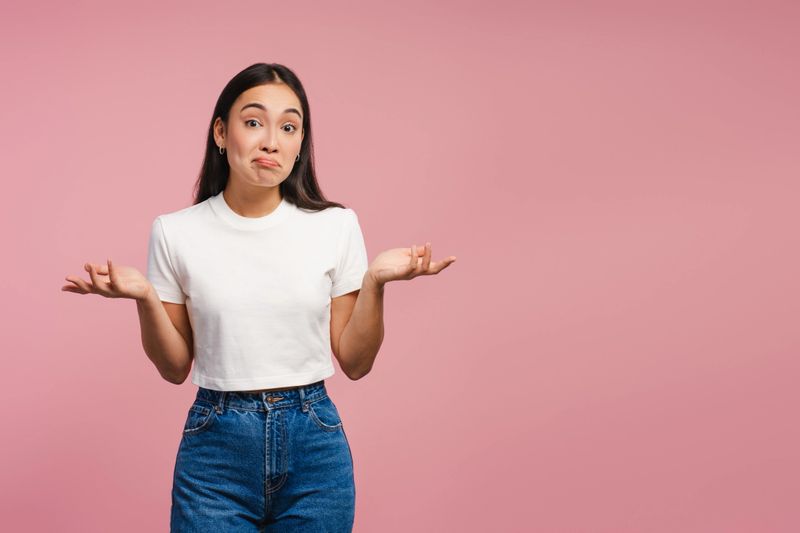 Confused young woman shrugging shoulders, looking at camera posing on pink background, copy space. Advertisement, shopping concept