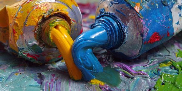 Yellow and blue paint squeezing out of tubes onto a colorful palette.