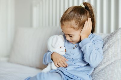 Child holding ear in pain while sitting on a couch.
