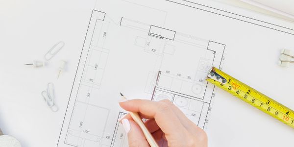 Hand sketching on architectural blueprint with measuring tape and office supplies nearby.
