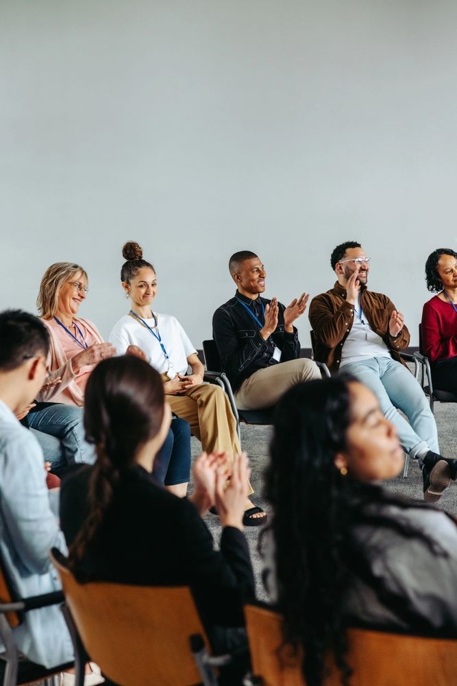 Diverse group of people sitting in a circle, clapping and smiling during a meeting.
