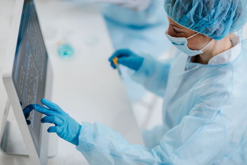 A young adult female lab technician in sterile attire examines specimens