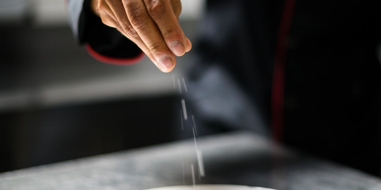 Hand sprinkling salt or seasoning over food in a kitchen.