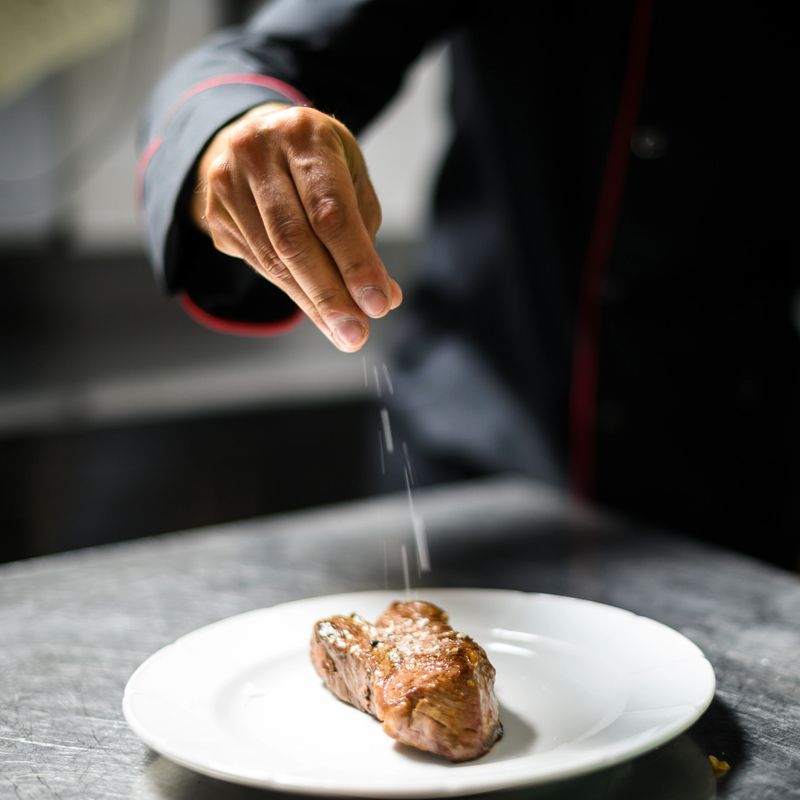 Chef expertly seasons a steak in a busy kitchen, creating a gourmet dish fit for fine dining