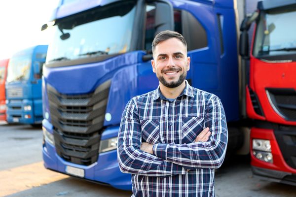 Smiling truck driver standing confidently with arms crossed in front of large trucks.