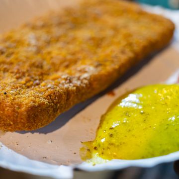 Close-up of a breaded fried cutlet with yellow mustard sauce on the side.