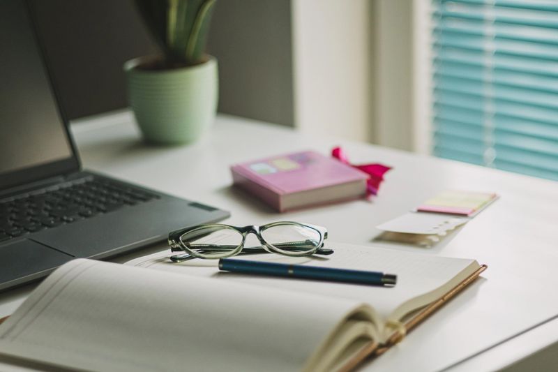 Women's office desk table. Laptop computer, cup of coffee,  reading glasses and office supplies.