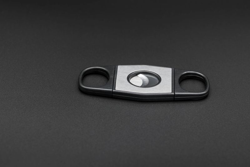 A close-up image of a stainless steel cigar cutter with a double blade design, displayed against a dark background. The sleek metal finish and minimalist aesthetic make this smoking accessory both functional and stylish, perfect for cigar enthusiasts. The dark backdrop emphasizes the sharpness and precision of the tool, making it ideal for luxury and tobacco-related themes.