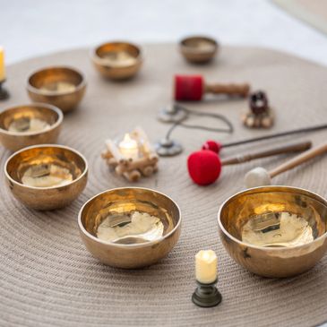 Set of brass singing bowls arranged on a mat with mallets and candles.