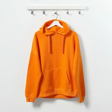 Bright orange hoodie hanging on a white wall hook rack.