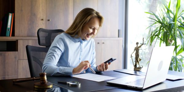 Mujer sonriente trabajando en oficina con documentos y teléfono.