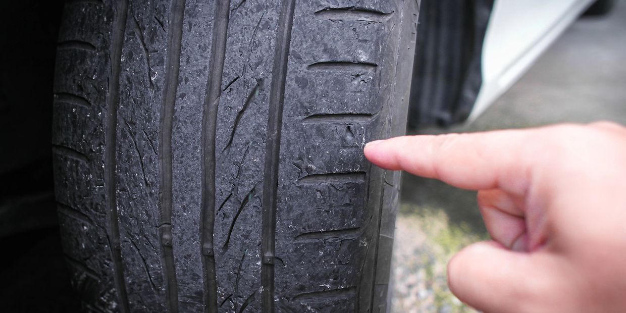 Finger pointing at a worn-out car tire with visible tread damage.