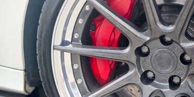 Close-up of a car wheel with a red brake caliper and drilled rotor.