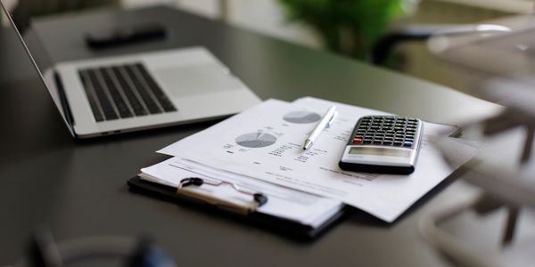 Calculator, pen, and financial charts on a desk near a laptop.