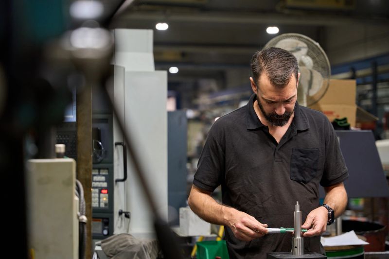 Metalworker carefully marking measurements on a custom mechanical part in a metallurgy factory, ensuring precise fabrication