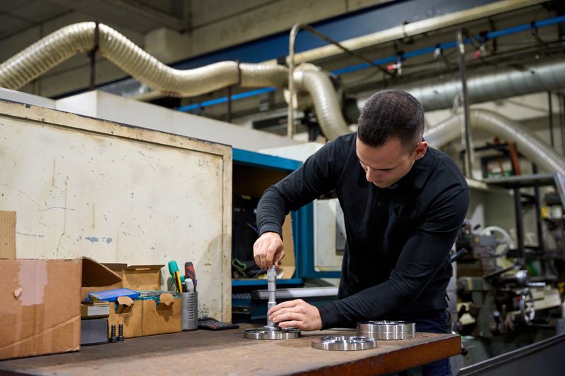 Metalworker carefully measuring custom mechanical parts using precision tools in a metallurgy factory, ensuring high quality and standards