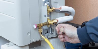Technician adjusting valves on an air conditioning unit outdoors.